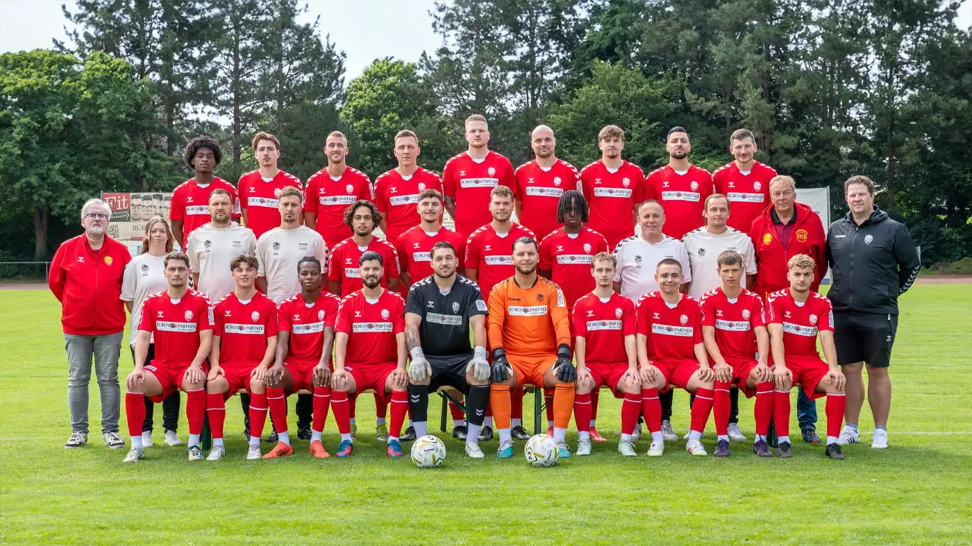 1. Herren in roten Trikots und Betreuer auf Rasen, Gruppenporträt.