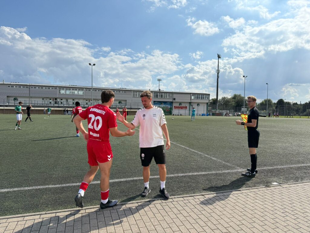 Fußballspieler Nr.20 in Rot bedankt sich beim Trainer am Spielfeldrand.