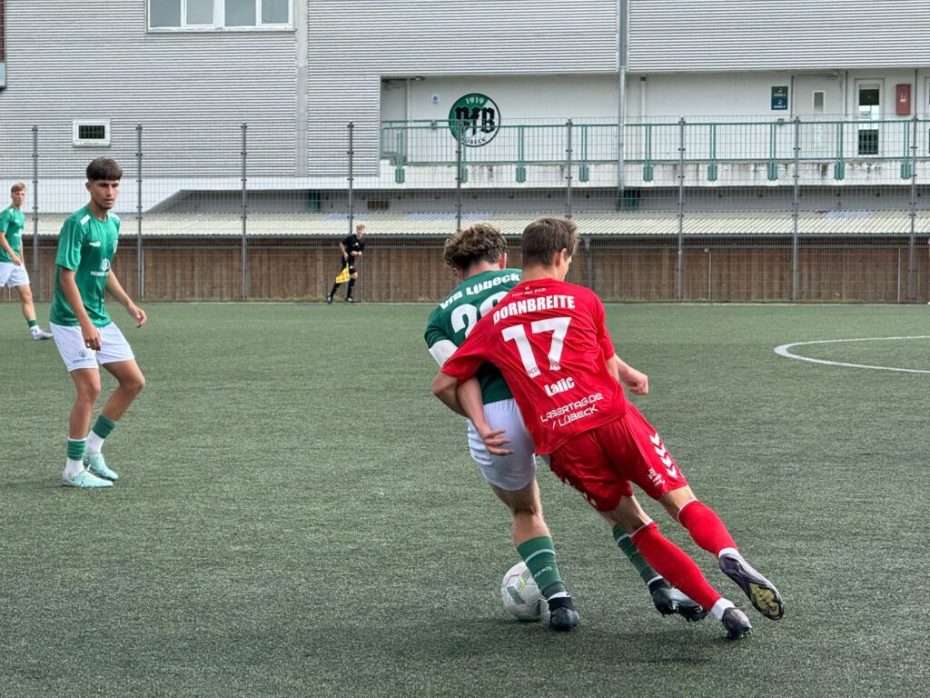 Spieler in Rot (Nr.17) drängt grünen Gegenspieler um den Ball auf dem Fußballfeld.