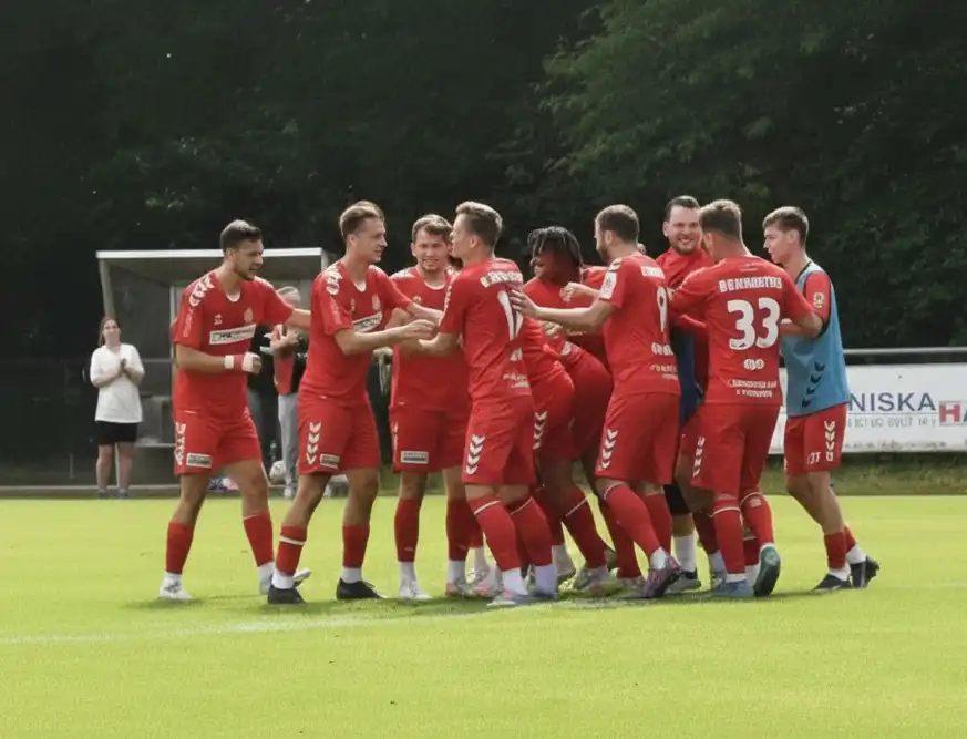 Männer-Fußballteam in roten Trikots umarmt sich jubelnd auf dem Spielfeld